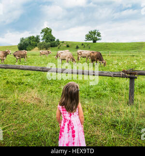 Vista reale di una ragazza guardando le mucche al pascolo in campo, Fuessen, Baviera, Germania Foto Stock