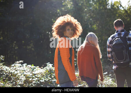 Donna escursioni con gli amici guardando sopra la spalla in telecamera Foto Stock