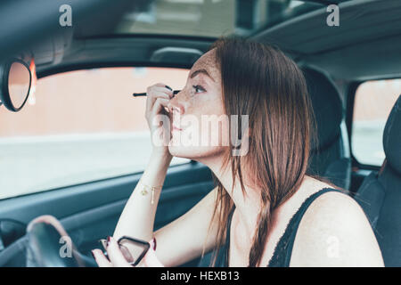 Giovane donna con lentiggini applicando ombretto in specchio auto Foto Stock