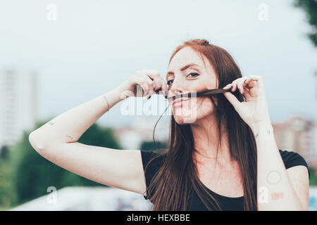 Ritratto di giovane donna con lentiggini rendendo i baffi con lunghi capelli rossi Foto Stock