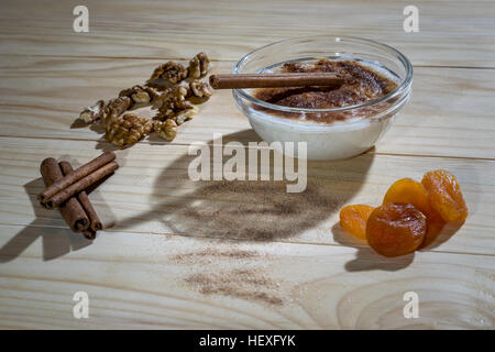 Cremoso budino di riso con bastoncini di cannella, noci e albicocche secche su di un tavolo di legno Foto Stock