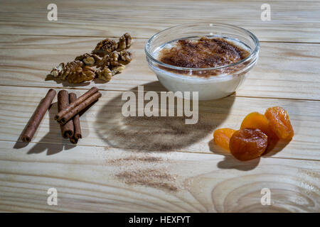 Cremoso budino di riso con bastoncini di cannella, noci e albicocche secche su di un tavolo di legno Foto Stock