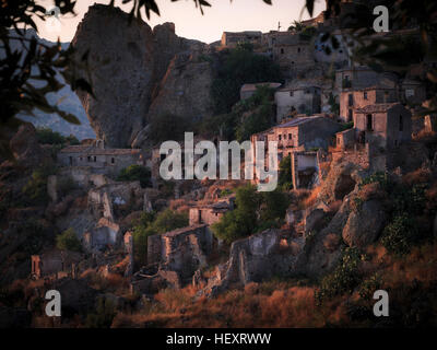 Il villaggio abbandonato di Pentedattilo al tramonto incorniciato da sfocato ulivo rami, Calabria, Italia. Foto Stock