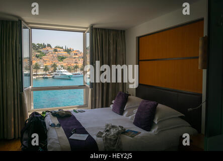 Guardando fuori della finestra sul bellissimo porto di Hvar, sull'isola di Hvar in Croazia, con un letto con la valigia, abbigliamento, Foto Stock