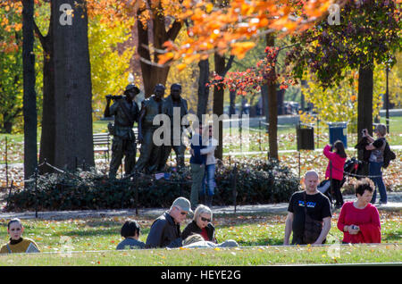 I visitatori in primo piano a piedi in discesa su un pendio la lettura dei nomi dalla parete presso il Memoriale dei Veterani del Vietnam a Washington DC. Foto Stock