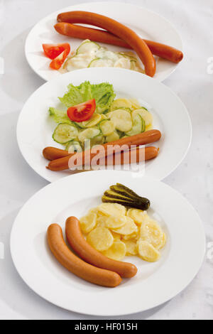 Tre piastre di salsicce e diversi tipi di insalata di patate Foto Stock