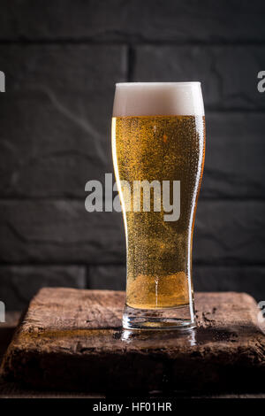 Bicchiere di birra chiara con bolle vicino muro nero Foto Stock