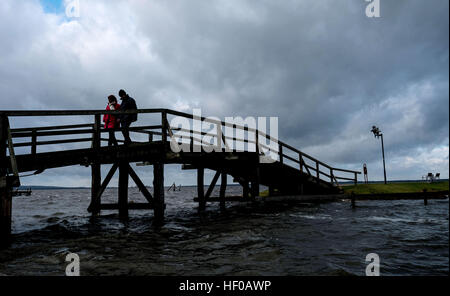 Steinhude, Germania. Il 26 dicembre, 2016. Nuvole scure può essere visto oltre la passerella sul Lago Steinhude in Steinhude, Germania, 26 dicembre 2016. Questo lunedì tempesta 'Barbara' attraversa la Germania con forti piovaschi, come riportato domenica dal tedesco servizio meteo di Offenbach. Mentre piovaschi sono possibili sulla costa, vi potrebbe essere estremamente raffiche di vento in montagna. Le temperature rimangono relativamente mite per dicembre 8 a 13 gradi celsius. Foto: Peter Steffen/dpa/Alamy Live News Foto Stock