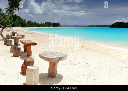 Serie di sgabelli in legno e tabelle per i visitatori posto sotto palme di cocco sulle sabbie bianche della spiaggia e di fronte Malet isola. Port Olry village Foto Stock