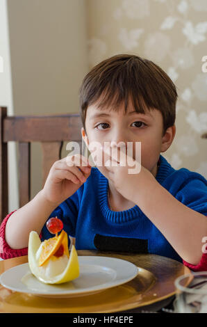 Un ragazzo si siede a un tavolo da pranzo di mangiare il melone. Foto Stock