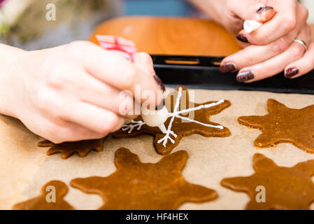 Mano Womans decorare i biscotti con lo zucchero. Rendendo Gingerbread Cookies serie. Foto Stock