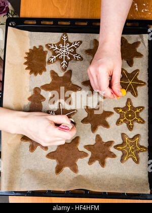 Mano Womans decorare i biscotti con lo zucchero. Rendendo Gingerbread Cookies serie. Foto Stock