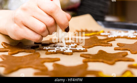 Mano Womans decorare i biscotti con lo zucchero. Rendendo Gingerbread Cookies serie. Foto Stock