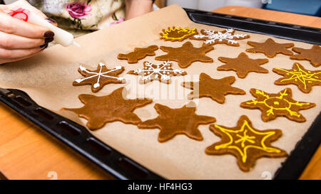 Mano Womans decorare i biscotti con lo zucchero. Rendendo Gingerbread Cookies serie. Foto Stock