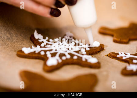 Mano Womans decorare i biscotti con lo zucchero. Rendendo Gingerbread Cookies serie. Foto Stock