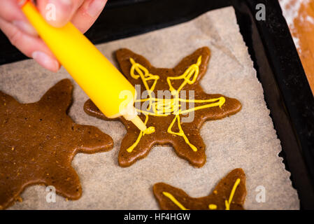 Mano Womans decorare i biscotti con lo zucchero. Rendendo Gingerbread Cookies serie. Foto Stock