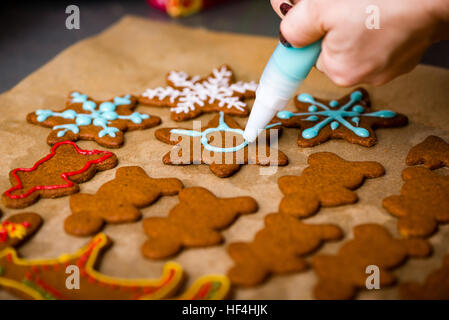 Mano Womans decorare i biscotti con lo zucchero. Rendendo Gingerbread Cookies serie. Foto Stock
