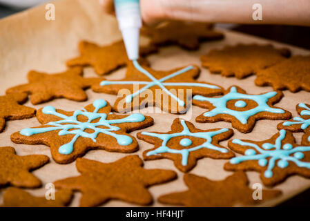 Mano Womans decorare i biscotti con lo zucchero. Rendendo Gingerbread Cookies serie. Foto Stock