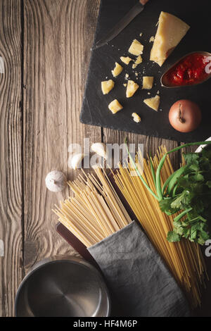 Gli ingredienti per cucinare gli spaghetti con formaggio ed erbe fresche sul vecchio tavolo in verticale Foto Stock