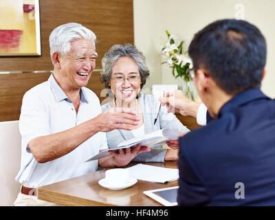 Felice senior asian giovane pronto a firmare il contratto di prendere una penna da un addetto alle vendite. Foto Stock