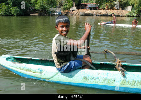 Bentota, Sri Lanka - 23 dicembre 2004: Ragazzo con una scimmia sguazzare nella sua canoa sulla laguna vicino a Bentota nello Sri Lanka Foto Stock