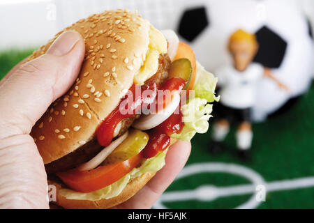 Mano che tiene un hamburger in un campo di calcio Foto Stock