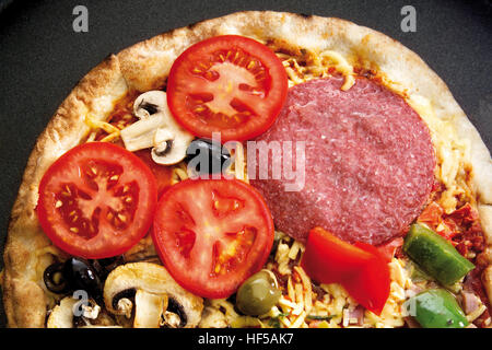 Pizza con salame, pomodori, olive, funghi e peperoni Foto Stock