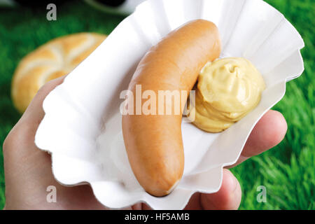 Mano azienda bockwurst salsiccia con senape sul piatto di carta Foto Stock