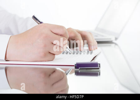 Imprenditore a scrivere una breve nota sul notebook aperto con penna e bicchieri. tono caldo. Foto Stock