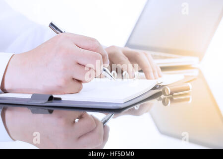 Imprenditore a scrivere una breve nota sul notebook aperto con penna e bicchieri. Foto Stock