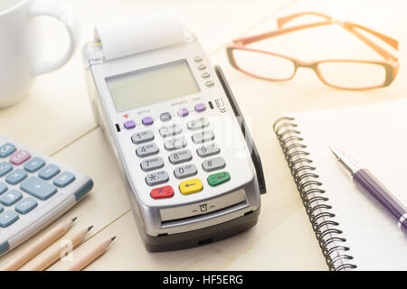 Terminale Carte di credito o EDC su cassa tavolo in legno nel negozio con carta di credito, penna, calcolatrice e bicchieri in background. Foto Stock