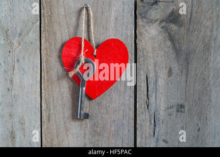 Chiave attaccata ad un cuore rosso con una stringa. Sfondo di legno Foto Stock