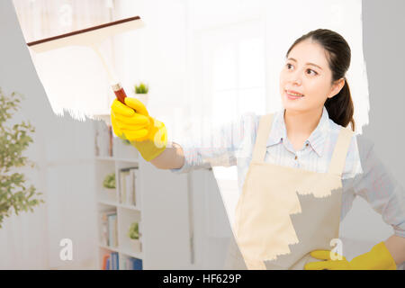 Donna felice in guanti finestra di pulizia con un panno a casa. Grande finestra in vetro espanso. Lavori di casa concetto. razza mista asiatica modello cinese. Foto Stock