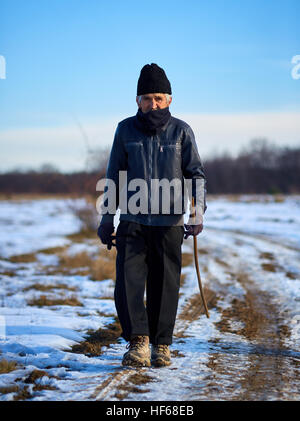 Vecchio contadino avente una passeggiata in campagna in una fredda giornata invernale Foto Stock