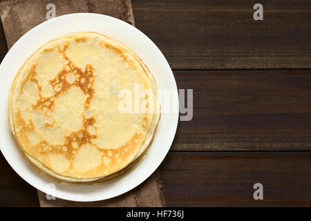 Appena sfornati crepes impilati sulla piastra, fotografato overhead sul legno scuro con luce naturale (messa a fuoco selettiva, messa a fuoco sulla parte superiore crêpe) Foto Stock