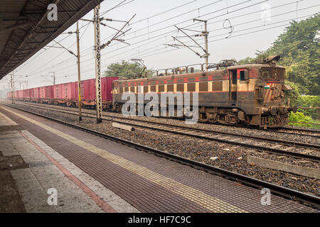 A goods train of the Indian railways crossing a deserted platform on a foggy winter morning. Foto Stock