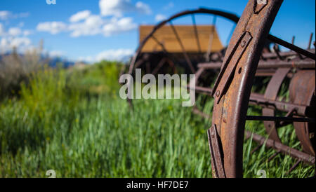 Agricoltura ranch sfondo con fienile e rusty farm aratro. Erba verde, blu cielo e fienile in legno. Profondità di campo con il focus sulla ruggine ruota dell'aratro. Foto Stock