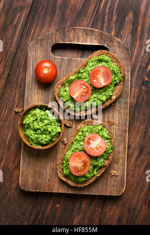 Pane con il pesto e pomodori in background in legno, vista dall'alto Foto Stock