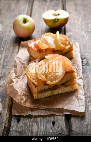 Mele caramellate su pane tostato su sfondo di legno Foto Stock