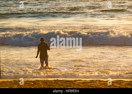 Un uomo più anziano in piedi su una spiaggia a pesca in surf con una canna da pesca sulla spiaggia di Sydney la mattina presto d'estate in Australia Foto Stock