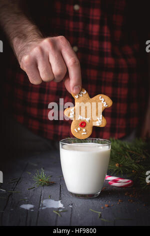 Gingerbread cookie e il latte. Uomo con gingerbread man cookie e andando a sprofondare in un bicchiere di latte. Natale arte cibo Foto Stock