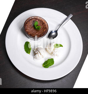 Riscaldare il dessert cioccolato fondente torta di lava servita con gelato alla vaniglia sfere e menta su piastra bianca. Famoso francese dessert sul legno scuro tabella vista dall'alto. Foto Stock