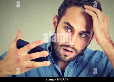 Preoccupato sconvolto l uomo sensazione di testa, sorpreso egli è la perdita di capelli, receding hairline, bad news isolato su sfondo grigio. Negativo espressione facciale Foto Stock