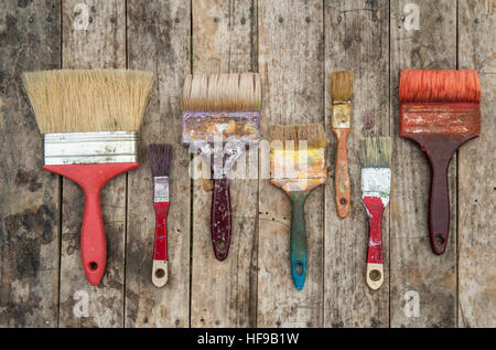 Set di pennelli utilizzati con i bit di vernice essiccata su uno sfondo di legno Foto Stock