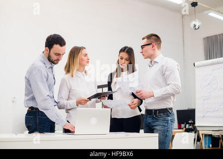 Giovane uomo a discutere di una ricerca di mercato con i colleghi in una riunione. Il team di professionisti di una conversazione in sala conferenze alla ricerca di documenti. Foto Stock