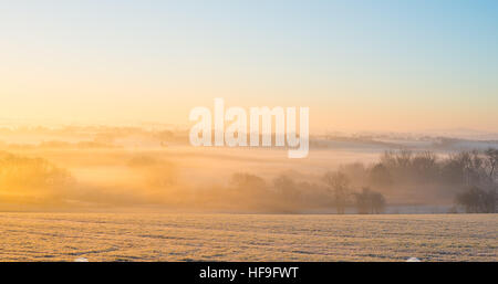 Sun sorge oltre la nebbia paesaggio rurale su un pupazzo di neve con inverni nitido mattina con una temperatura di -6 ºC vicino a Warwick, Warwickshire, Regno Unito Foto Stock