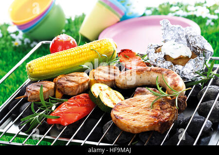 Barbecue scena: salsicce fritte, spiedino di filetto, tritare la carne di maiale, patate avvolti in carta metallizzata con dip, tutolo di mais, capsicum e pomodoro Foto Stock