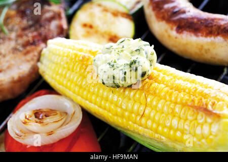 Scena di barbecue, tutolo di mais con una cucchiaiata di burro alle erbe in primo piano Foto Stock