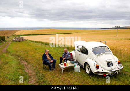 Due turisti olandesi hanno un picnic accanto alla loro VW Beetle in un campo vicino a St Abbs, Berwickshire, Scottish Borders, Scotland, Regno Unito Foto Stock