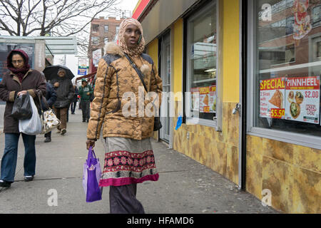 Un africano donna musulmana che indossa un hijab con un cellulare premuto al suo orecchio sul 35th Avenue a Jackson Heights, Queens, a New York Foto Stock